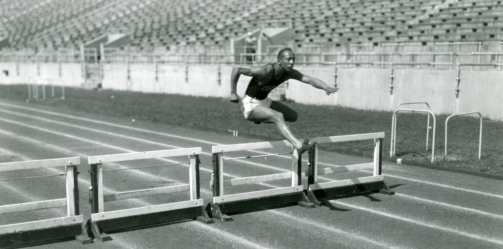 Jesse Owens jumping over a hurdle during practice at Ohio Stadium, side view, 1936